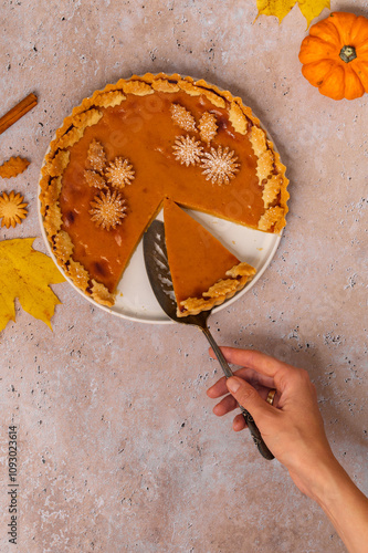 Traditional Pumpkin Pie for Thanksgiving dinner with decorative pumpkins and leaves. Homemade pastry. Woman serving Holiday dessert. A piece of Pumpkin Pie.