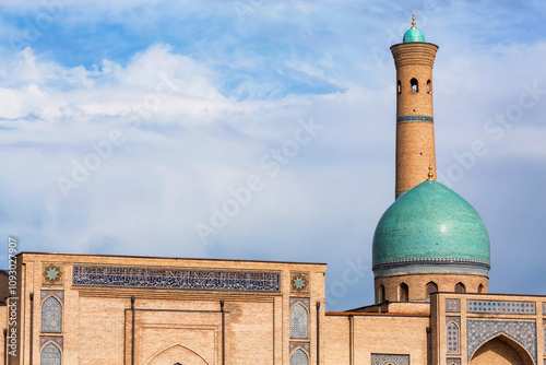 View of the Hazrati Imam Mosque in Tashkent, featuring its iconic turquoise dome and tall brick minaret against a blue sky. Tashkent, Uzbekistan