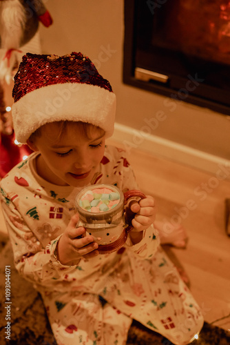 7-Year-Old Boy in Festive Pajamas Enjoying Hot Cocoa by a Fireplace in a Cozy Christmas Setting 