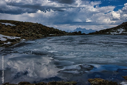 Serene frozen lake with dramatic clouds and peaks.