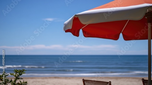 Vibrant red and white sun umbrella overlooking a serene beach with gently lapping ocean waves under a clear blue sky.