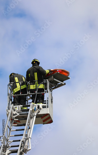 firefighters above the metal basket of the aerial ladder with the stretcher to transport the injured person