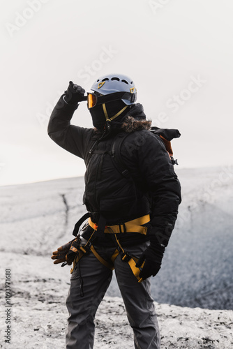 Mountaineer wearing protective gear, adjusting goggles while standing on snowy mountain peak, observing surroundings