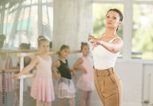 Girls student look at choreographer and memorize technique of performing ballet elements movements. Female master class with experienced coach. Teacher performs excerpt of dance in front of students