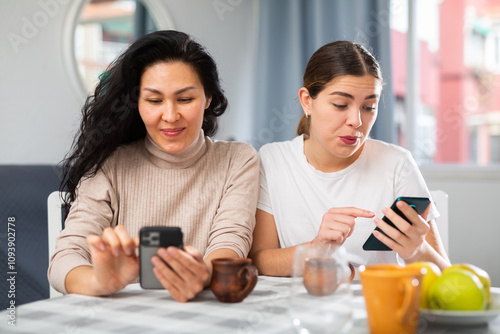 Positive adult girlfriends typing text on phone and talking on the speakerphone