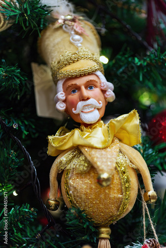 Christmas nutcracker featuring a golden, royal-inspired toy with a cheerful expression, hangs on a festive green Christmas tree. Figurine of a wooden New Year's nutcracker with a white beard in a suit