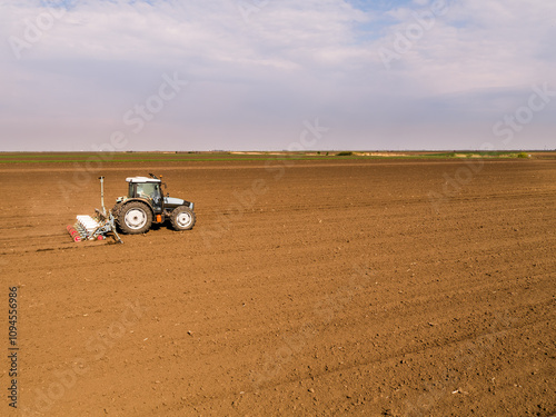 Tractor seeding crops in plowed field, agriculture industry