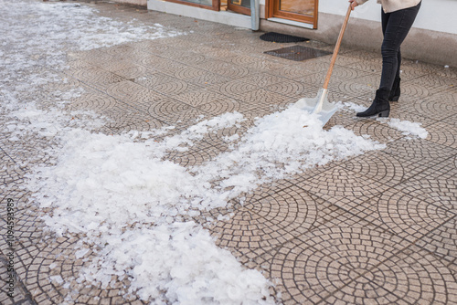 A person shoveling ice from a patterned tiled surface during winter. The scene captures the effort of clearing snow and ice from a walkway, emphasizing winter maintenance and safety.