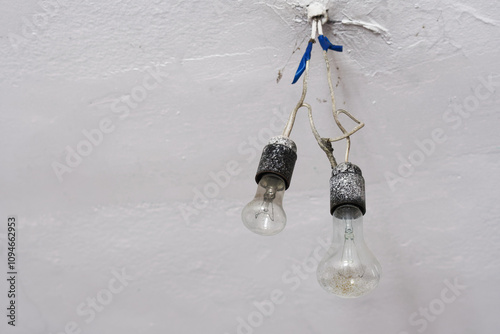 Old worn out light bulbs installed in a socket on the whitewashed ceiling of an abandoned room. Photo