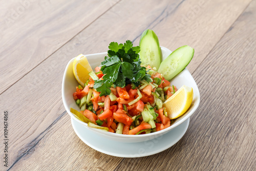 Fresh Vegetable Salad including green chilli, cabbage, tomatoes, cucumbers, lemon and coriander served in a white bowl isolated on wooden table side view of arabic salad