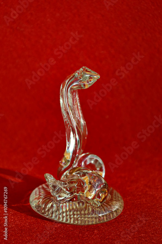 the symbol of the new year 2025. crystal snake figurine on a red background. a transparent cobra. Happy New Year. background for decoration. winter holiday.