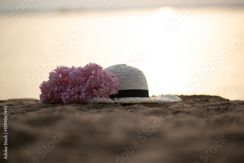 a hat with fresh flowers lies on the sand against the background of the sea