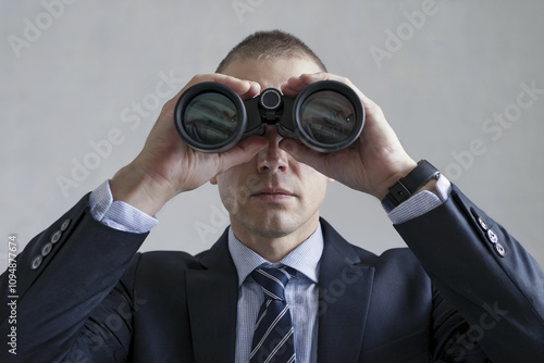 Man in a shirt and tie is spying on someone through binoculars.