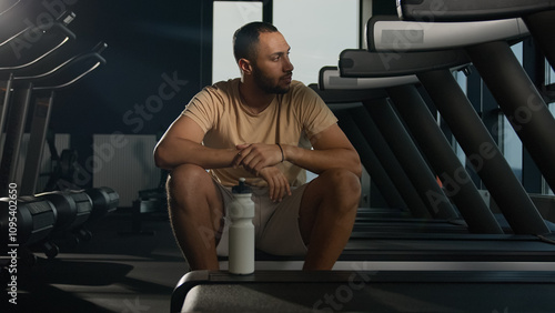 Tired African American man sit on treadmill relax after hard physical workout cardio training in fitness club gym exhausted sweaty sportsman runner thirsty drink water sport bottle healthy lifestyle