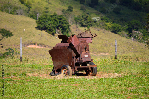 An antique wheat thresher in a rustic outdoor setting. The old agricultural machinery, with metal and wooden parts, shows vintage craftsmanship, contrasting with the natural background.