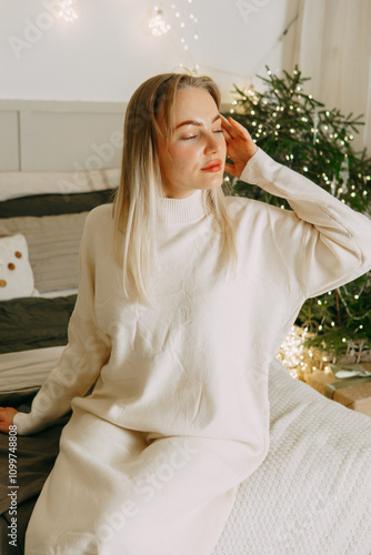 A blonde woman on a bed in a Scandinavian interior decorated for Christmas. A Christmas gift in a craft package. The period of the winter New Year holidays.