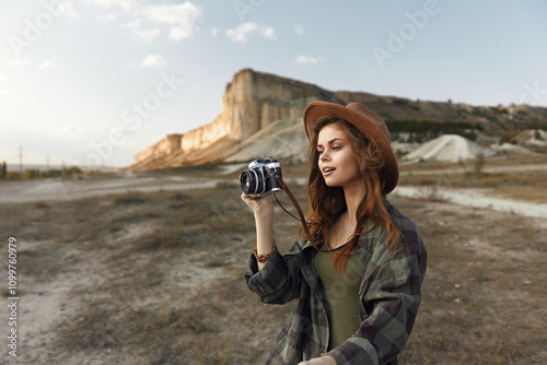 Desert adventure woman in hat captures the scenic beauty with vintage camera amid the arid landscape