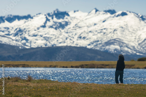 A woman meditating by a mountain lagoon (Caña el Gallo) observes a snowy range in the background (Gredos), blurred in the distance, and seems completely overwhelmed by the view