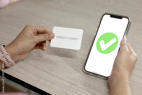 A person holding a credit card next to a smartphone displaying a green checkmark, symbolizing a successful online payment transaction.