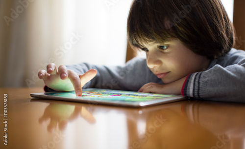 A young child focuses intently on a colorful tablet screen while sitting at a wooden table. Natural light illuminates the scene, creating a warm atmosphere for play and learning.