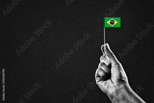 Hand in Black and White Holding Brazil Flag, Black Textured Background with Copy Space