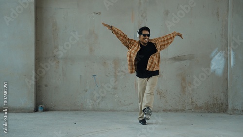 Attractive hispanic dancer in casual look practice street dance while listen music from headphone at cement background. Motion shot of break dancing performance. Outdoor sport 2024. Hiphop.