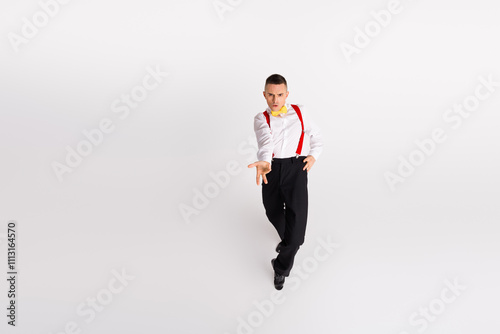 Young man in elegant attire dances with energy and style on a white background