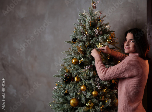 Cute young dark-haired girl decorating Christmas tree with toys, space for text, advertising and discounts, copy space.