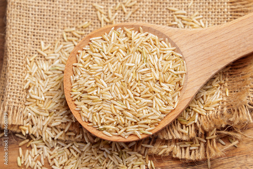 Organic uncooked basmati rice placed in a wooden spoon on burlap fabric and rustic board surface. Natural texture of long-grain gluten-free ingredient. Close up. Top view