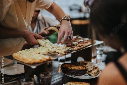 A group of people enjoying various flat bread pizzas at a buzzing social dinner. The setting conveys a sense of community and enjoyment around a shared meal.