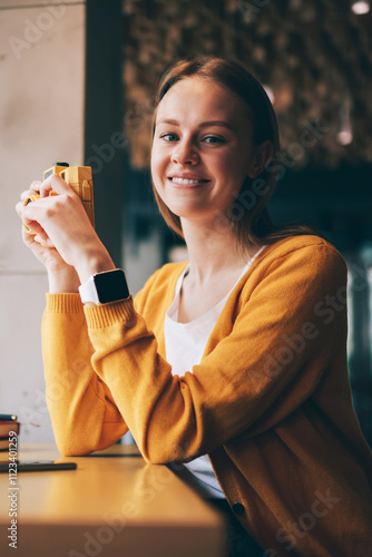 Portrait of cheerful woman feeling excited of photography hobby in cozy cafeteria recalls of beautiful moments, happy hipster girl looking at camera while holding vintage equipment in hands indoors