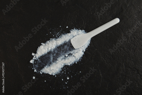 Colloidal silicon dioxide and plastic spatula on dark stone surface. Food additive E551. Enterosorbent. Silicon dioxide powder or Silica is used in medicine and food industry.