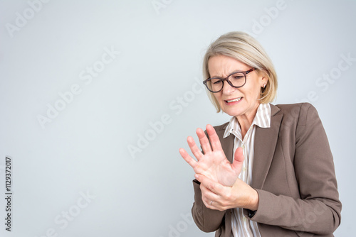 Elderly businesswoman applying moisturizing lotion cream on hand palm, easing aches. Senior lady experiencing severe arthritis rheumatics pains, massaging, warming up arm.