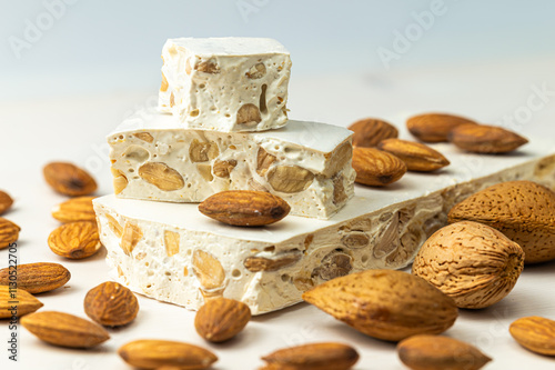 Pieces of hard nougat with almonds, with almonds next to it, on a light wooden surface. 